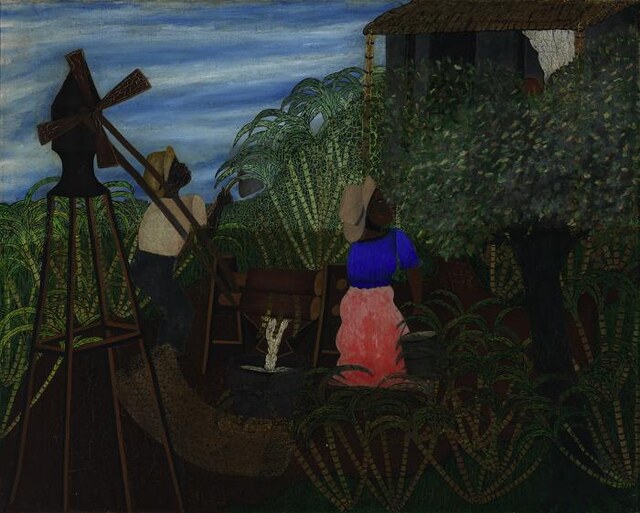 Homem e mulher de blusa azul e saia rosa trabalham numa moenda de cana, entre folhas altas, com uma casa ao fundo e uma vasilha sob o equipamento.