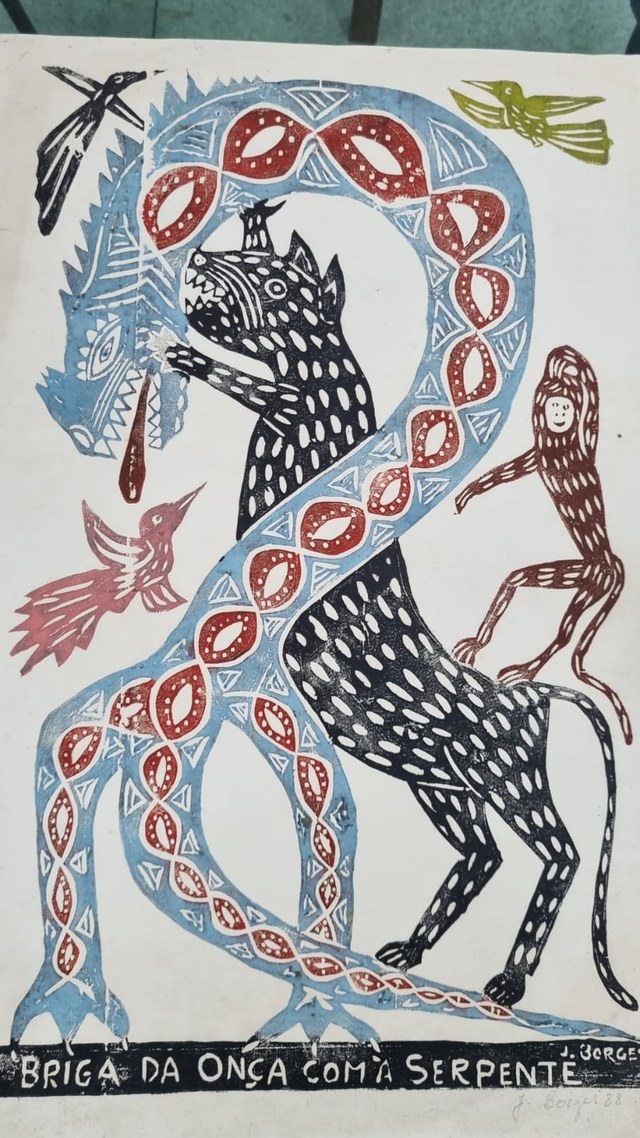 Uma onça preta de pé, com manchas brancas e a boca aberta, enfrenta uma serpente azul com desenhos vermelhos que se enrola ao redor dela; aves e uma figura pequena ocupam os espaços laterais.