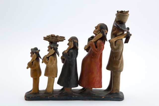 Cinco figuras de barro pintado caminham de perfil na mesma direção, da menor à maior; levam ferramentas nos ombros e cargas na cabeça, com duas mulheres ao centro e homens de chapéu nas extremidades.